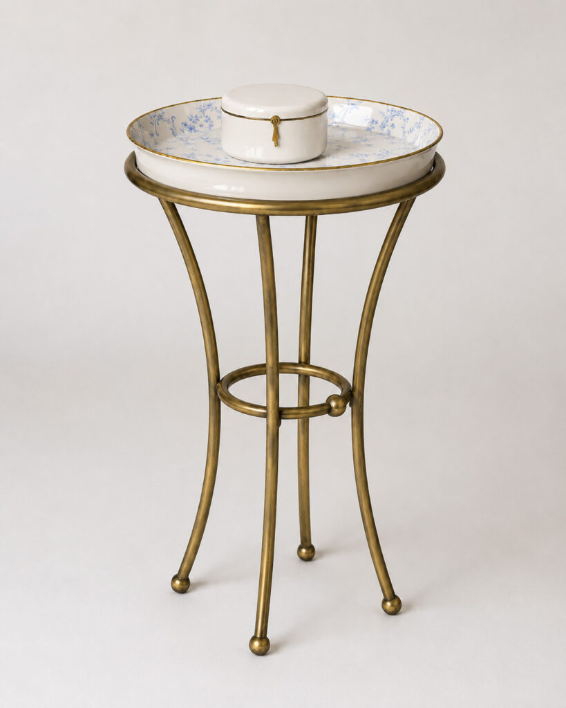 Round side table with a slender antique brass frame and a porcelain tray top with blue floral decoration, styled with a matching lidded porcelain box on a white background
