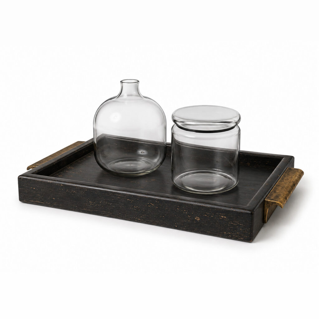 Decorative tray set with a painted wooden tray with patina, brass handles, a clear glass bottle and a lidded glass jar on a white background.
